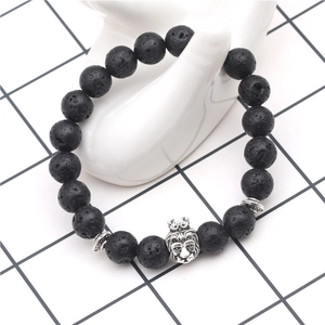 Detail of a black lava rock bead bracelet featuring a silver-tone lion head on a hand model