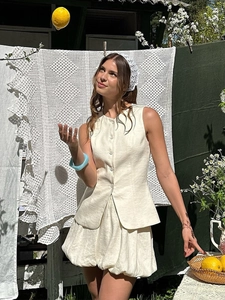 Détail du gilet crème sans manches boutonné et de la mini-jupe bouffante assortie en lin