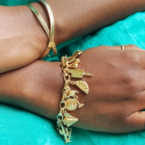 Gold charm bracelet with fruit and food pendants on a model wrist over green fabric