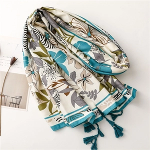 Detail of floral printed scarf with blue tassels and twill fabric texture on white surface
