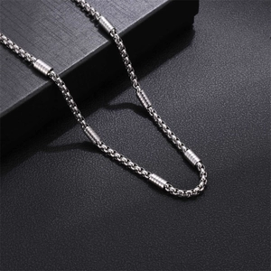 Silver stainless steel box chain necklace with cylindrical beads on a black box
