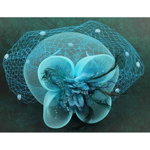 Top view of a teal bridal fascinator with mesh veil and feathers on green marble surface