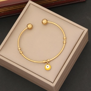 Macro view of golden stainless steel open cuff bracelet with yellow evil eye charm detail