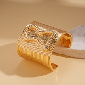 Detail of wide gold cuff bracelet with vertical textures and hourglass relief on stone