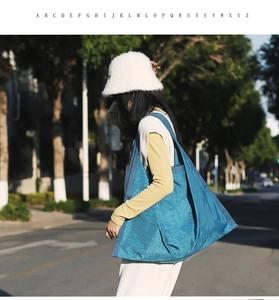 Blue slouchy nylon tote bag shown in an outdoor street style photoshoot on a model