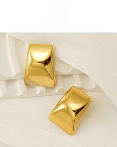 Détail de boucles d'oreilles rectangulaires en acier titane doré sur tissu en soie