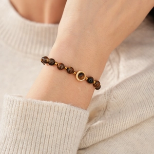 Détail du bracelet en perles d'oeil de tigre avec breloque dorée sur pull en maille