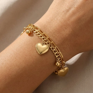 Close-up of gold layered heart charm bracelet worn on wrist with elegant pearl bead accents