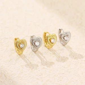 Close-up of heart-shaped gold and silver earrings with striped texture and zircon stone