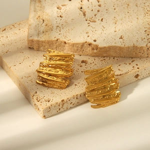 Détails de boucles d'oreilles dorées irrégulières avec texture martelée sur travertin