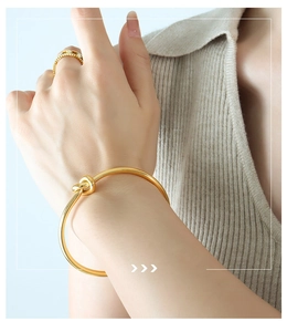 Detail shot of a minimalist gold knot bangle and matching ring on a female model