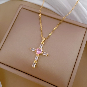 Elegant gold cross necklace with pink heart gem and baguette crystals on silk background