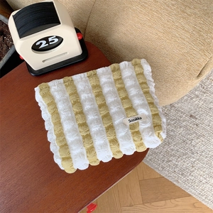 Macro shot of yellow and white striped bubble fabric makeup bag on dark wooden desk