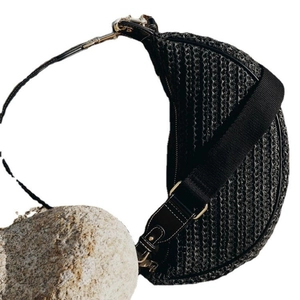 Black woven half-moon crossbody bag with wide strap displayed on a natural stone