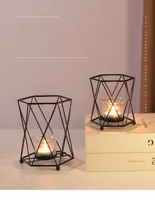 Detail of two black geometric iron candle holders with glass cups and burning tea lights