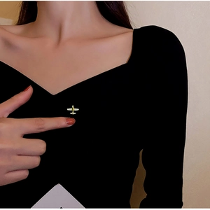 Minimalist golden airplane brooch pinned as a decorative accent on a black V-neck top