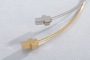 Macro detail of intertwined gold and silver bangle featuring polished cross charms