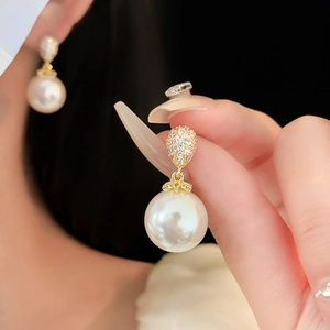 Dettaglio di orecchino a goccia con perla tonda e zircone con finitura dorata