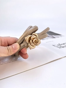 Detailed close-up of slim beige leather belt featuring a golden rose flower buckle