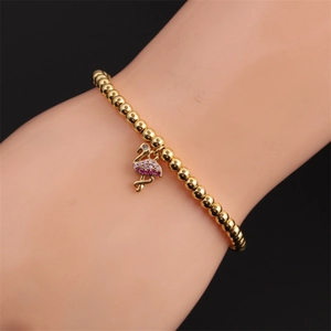 Détail d'un bracelet à billes dorées avec un pendentif flamant rose serti au poignet