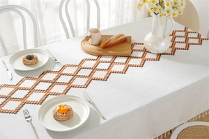 Detail of beige linen tablecloth featuring brown geometric embroidery and elegant tassels