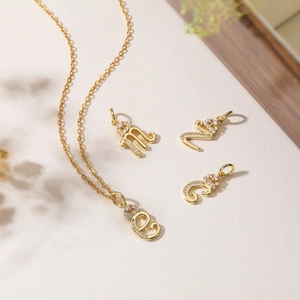 Gold plated initial letter pendants with micro-set zircon on elegant beige background