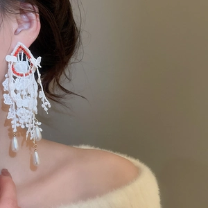 Close-up of white lace tassel earrings with red beads and hanging teardrop pearls