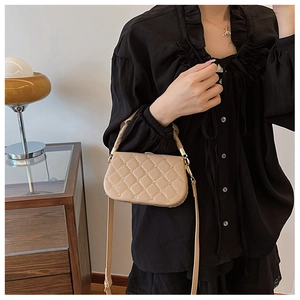 Detail of beige quilted crossbody bag featuring a gold clasp and chain strap on a model