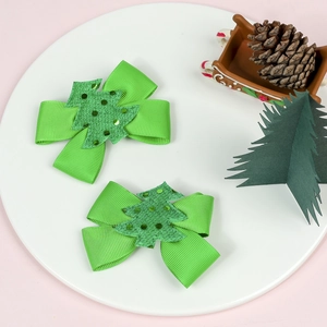 Set of 2 green Christmas bow hair clips with glitter tree decor on a white plate
