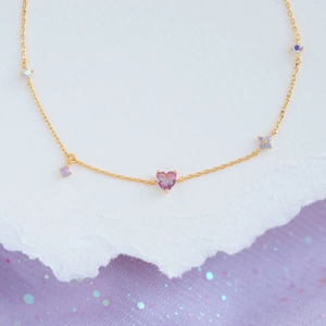 Detailed macro view of heart-shaped pink gemstone bracelet with gold chain and floral accents