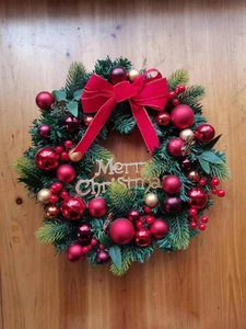 Detail of Christmas wreath with red bow, golden baubles and Merry Christmas sign