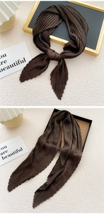 Detail of dark brown pleated silk scarf with accordion texture on a minimalist tray