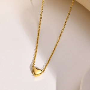 Macro detail of a 3D heart-shaped gold necklace pendant with smooth metallic texture