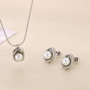 Detail of silver titanium chain necklace and shell pearl earrings set on beige fabric