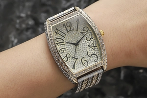 Close-up of a gold tonneau-shaped watch with crystal encrustation worn on a wrist