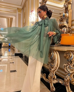 Detail of emerald green chiffon sheer blouse styled with elegant gold accessories