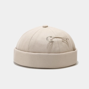 Detailed close-up of beige docker hat showing silver metal pin and thick twill texture