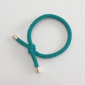 Detail of dark green woven elastic hair tie with textured knot and gold metal cylinders