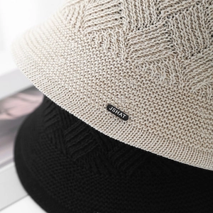 Close-up of knit bucket hats in beige and black with detailed JSHAT brand metal plaque