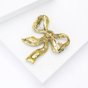 Detailed back view of the golden bow brooch showing the safety pin and metal texture
