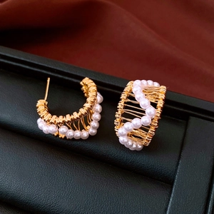 Macro view of C-shaped 18k gold-plated hoop earrings with intricate pearl weaving