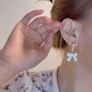 Detail of long bowknot pearl earrings hanging from the ear on a female model