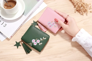 Close-up of floral embroidery on pink and green zip wallets with tassel and star charms