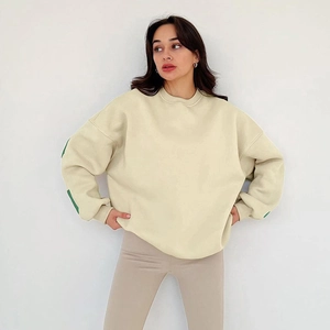 Détail du sweat-shirt beige oversize avec rayures vertes aux manches et texture en coton doux
