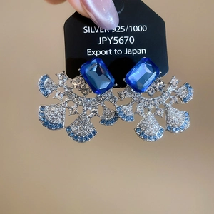 Detail of fan-shaped silver earrings with blue rectangular stones and pave diamonds