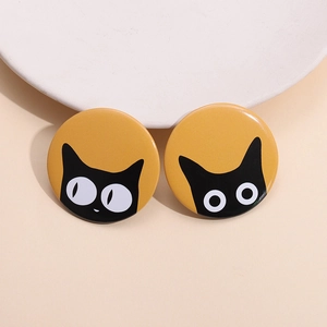 Close-up of two round tinplate badges featuring minimalist black cat illustrations