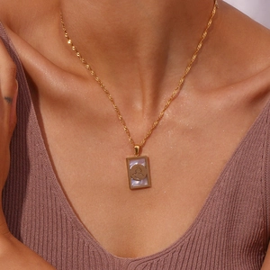 Primo piano della collana dorata con pendente rettangolare in madreperla su modella