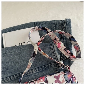 Close-up of stylish white shoulder bag with colorful butterfly patterns on denim jeans