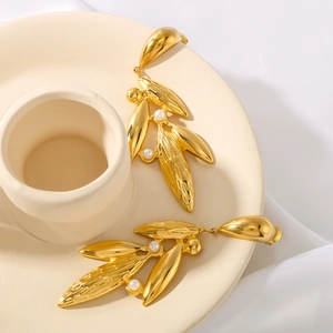 Polished 18k gold leaf earrings with pearls displayed on minimalist ceramic tray