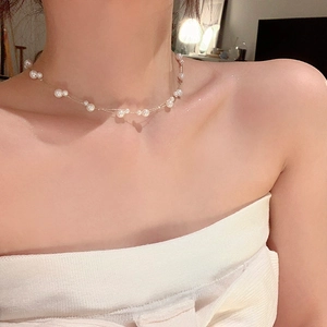 Detail showing double-layered pearl choker on model collarbone with warm lighting